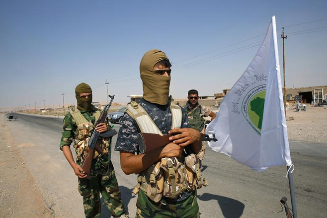 Fighters from the Shi'ite Badr Brigade militia stand near their flag as they guard at a checkpoint outside the town of Sulaiman Pek